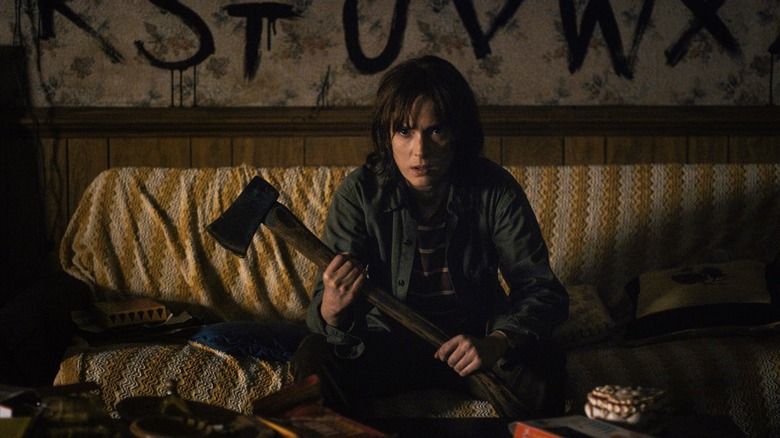 Winona Ryder sits holding an axe and glaring into the camera in Stranger Things.