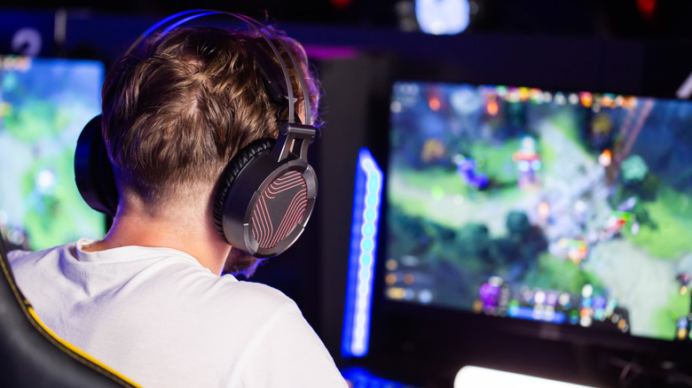 A person wearing large gaming headphones sits in front of a computer playing competitively at an event.