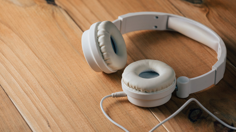 Off-white headphones with removable cable lay on a wooden surface.