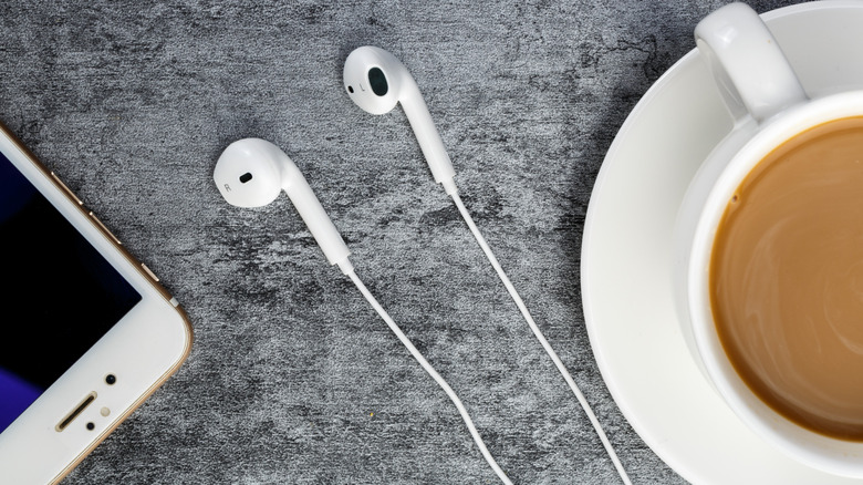 Wired earbuds between a phone and cup of coffee.