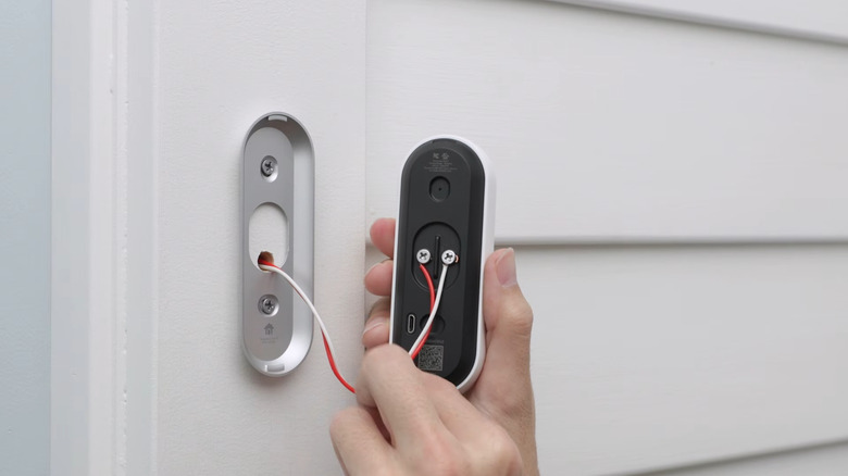 Hand holding Google Nest wired video doorbell connected to housing wires