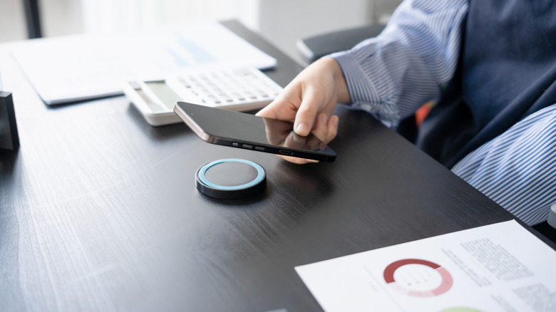 A man at a desk putting a phone on a wireless charger.