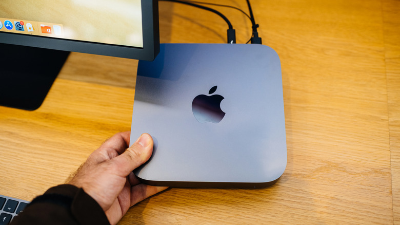 Person holding a Mac Mini over a desk.
