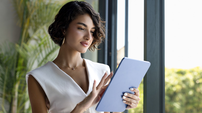A woman standing in front of a window using a tablet