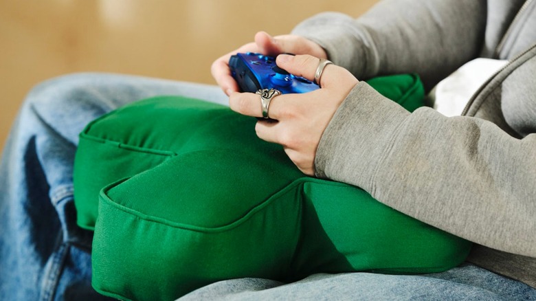 A person resting their hands and Xbox controller on a D-pad-shaped cushion.