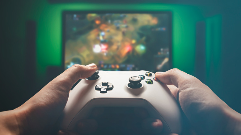person holding an xbox controller in front of entertainment center, green lighting around