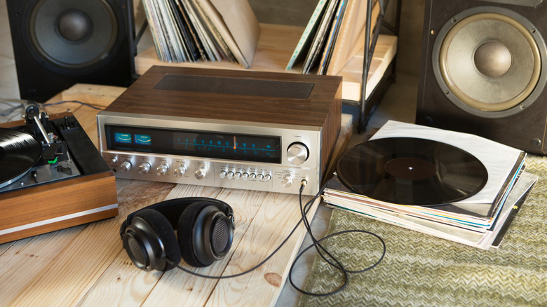 A silver hi-fi system sits on the floor next to a turntable, speakers, vinyl records, and a pair of black headphones