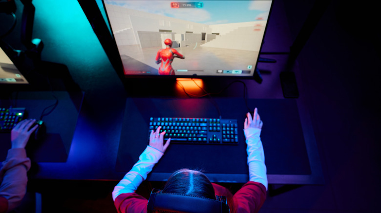 Gamer sitting at desk with monitor displaying a third-person shooter.