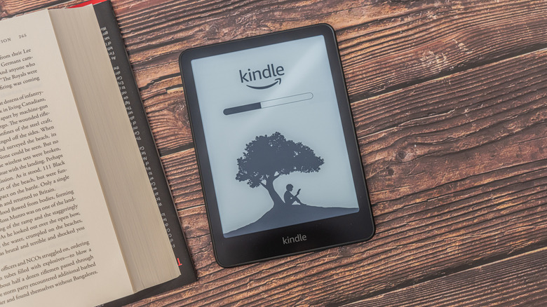 The Kindle Paperwhite laying on a wooden table next to an actual book.