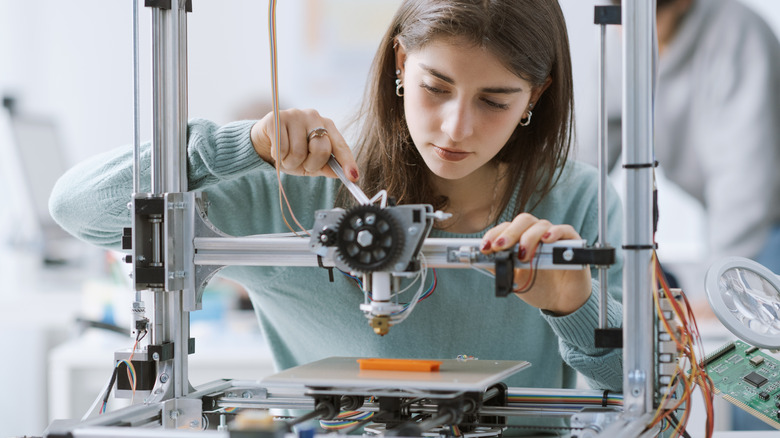 Someone making adjustments to a 3D printer.