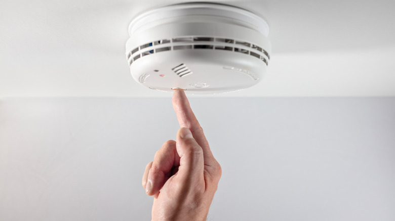 Close-up of hand pressing button on smoke detector