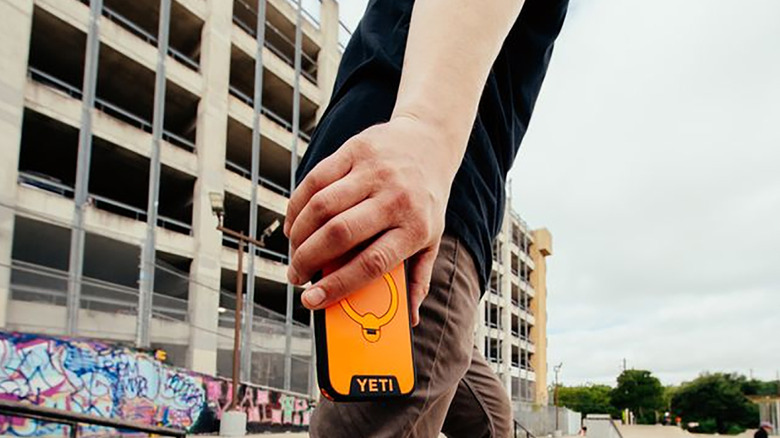 A person's hand by their waist holding a Yeti LoadOut iPhone case in orange.