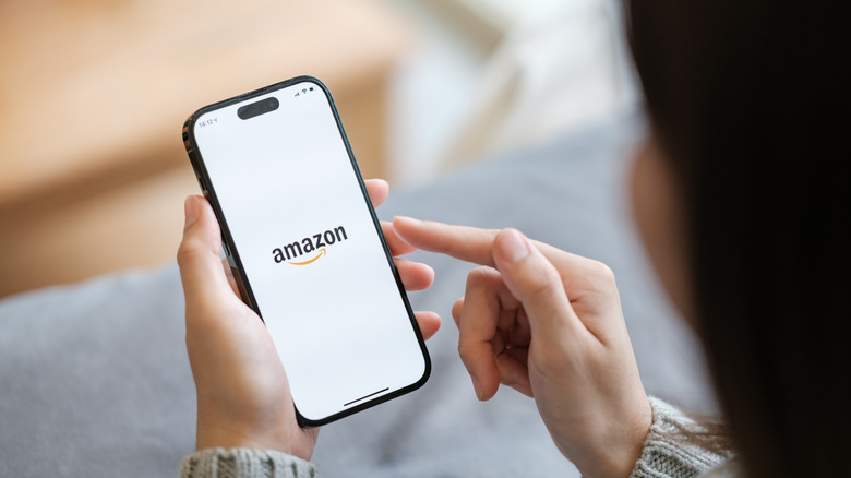 A woman holding an iPhone 14 model with the Amazon app loading.