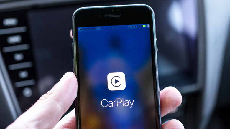 An iPhone held by a hand with the Apple CarPlay logo showing on the screen.
