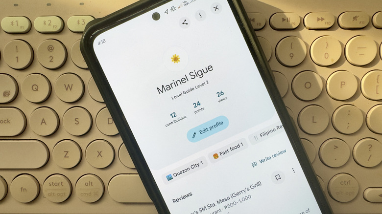 A phone showing the Google Maps Local Guides level and reviews with a keyboard in the background