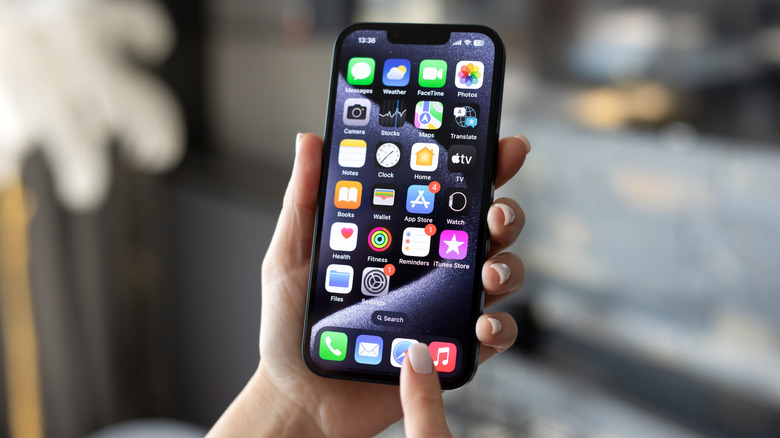 An individual holding an iPhone in their left hand, the index finger of their right hand hovering over the Safari icon on the iPhone Home screen