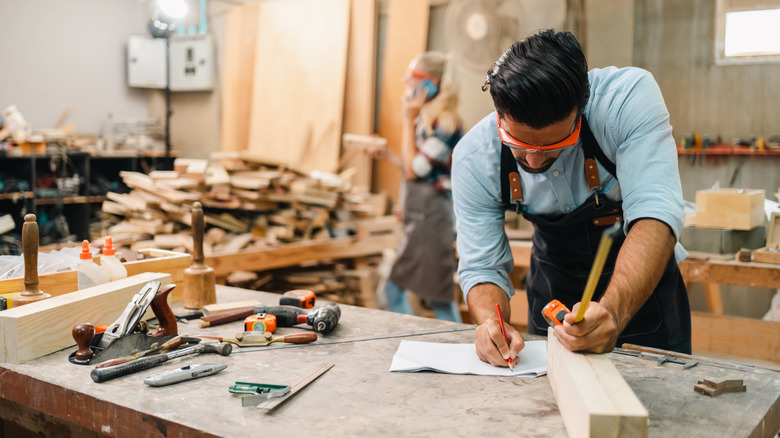 Man in wood working shop measuring boards.
