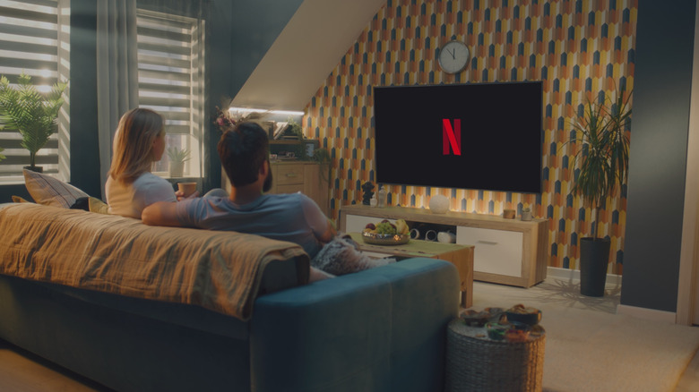 A couple seated on a sofa, looking at a TV showing the Netflix logo.