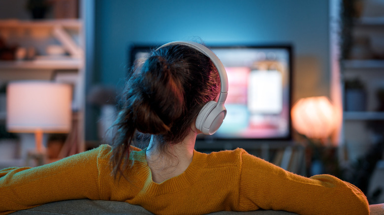 A woman wearing headphones and watching the TV.
