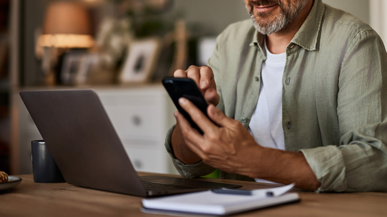Man using phone in front of laptop
