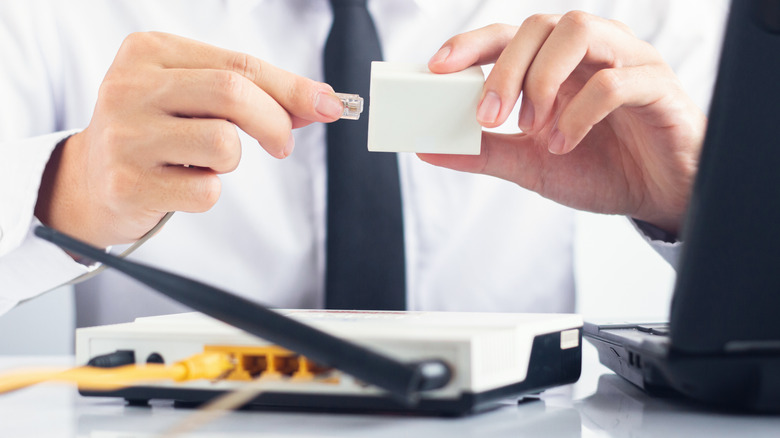 Man in tie plugging in RJ11 telephone cable with Ethernet adapter.