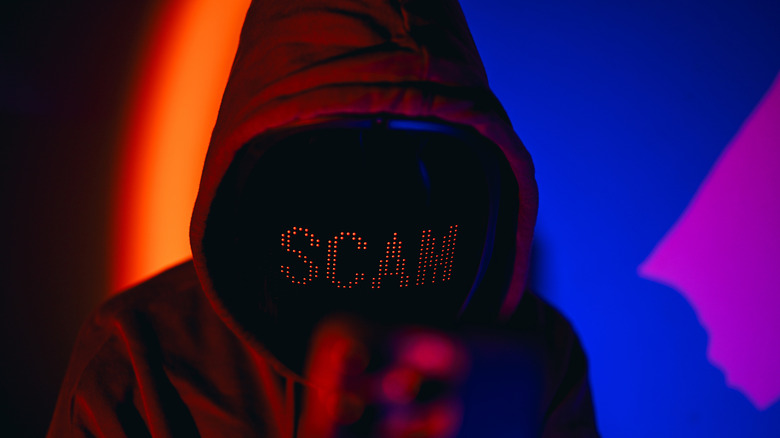 A hooded character with the word SCAM written across his face stands before a colorful background.