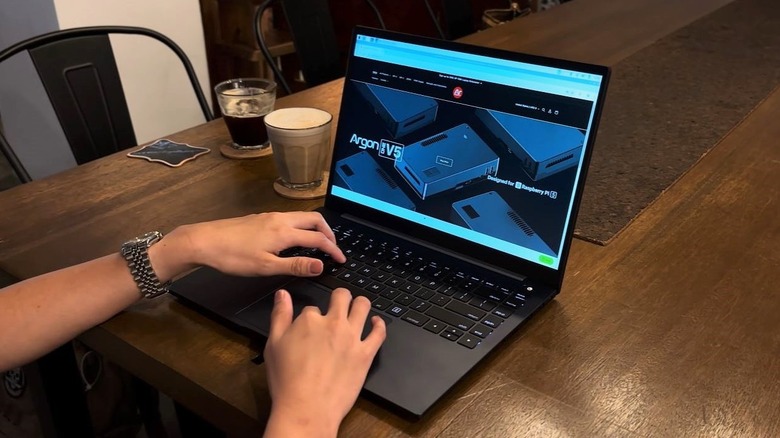 The Argon One Up Raspberry Pi CM5 laptop on a brown table beside two cups of coffee.