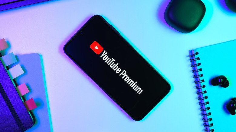 A cellphone laying on a desk in between two different notebooks, the cellphone is displaying the YouTube Premium logo