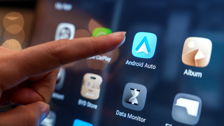 Close-up of a finger  tapping the Android Auto icon on a vehicle dash display.
