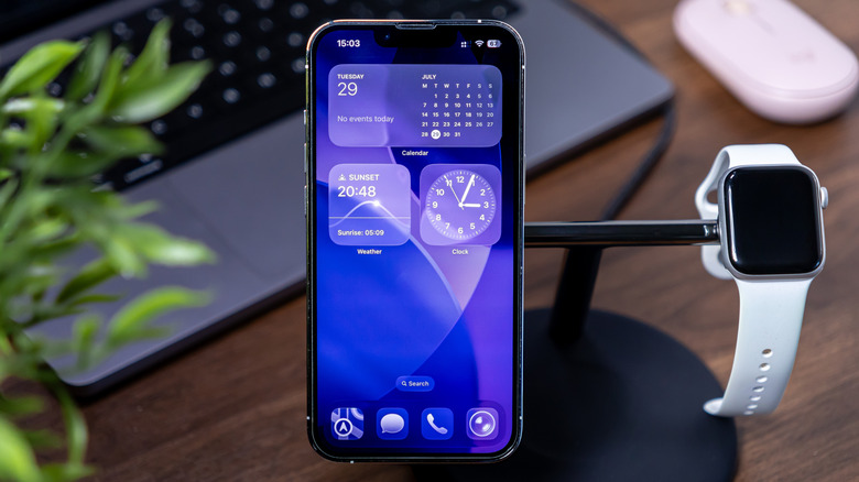 An iPhone rests atop a charging stand next to an Apple Watch