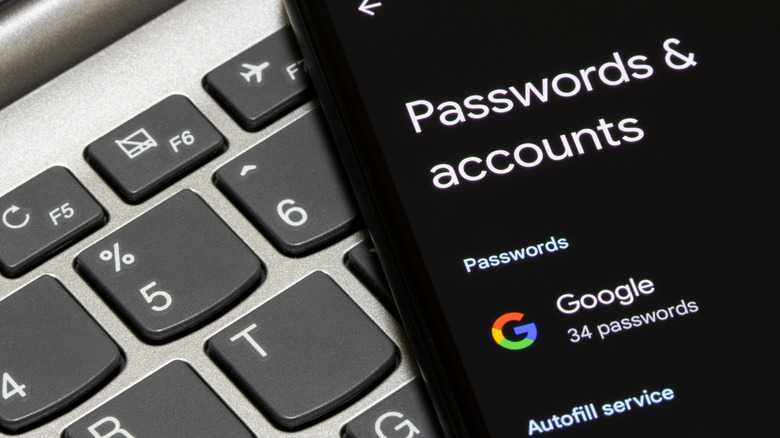 A phone lying atop a laptop showing saved passwords and accounts in a Google Account
