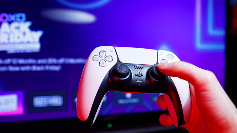 Person holding PlayStation 5 Dualsense controller with blurred TV screen in the background