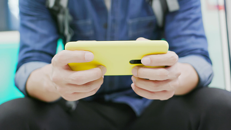 A person playing games on a phone in a yellow case.