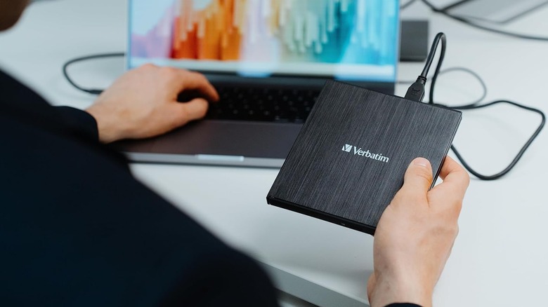 A person holding a Verbatim external Blu-ray player connected to a laptop.