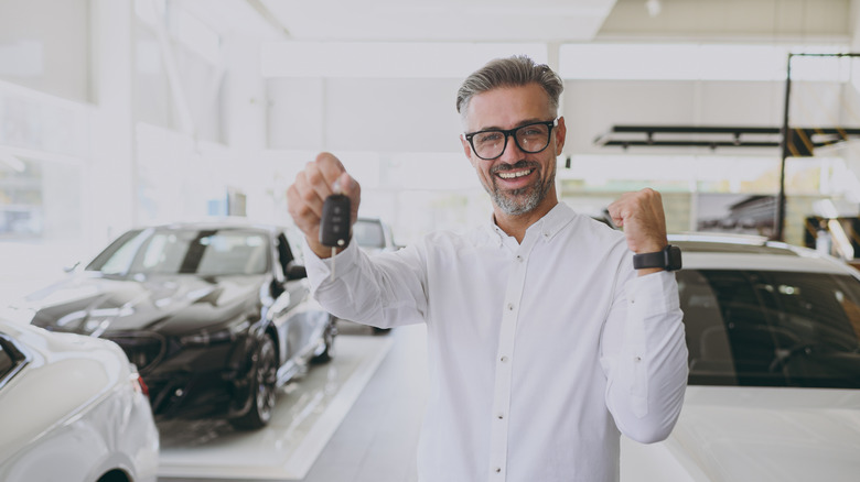 A man smiling as he holds a key fob in front of several cars