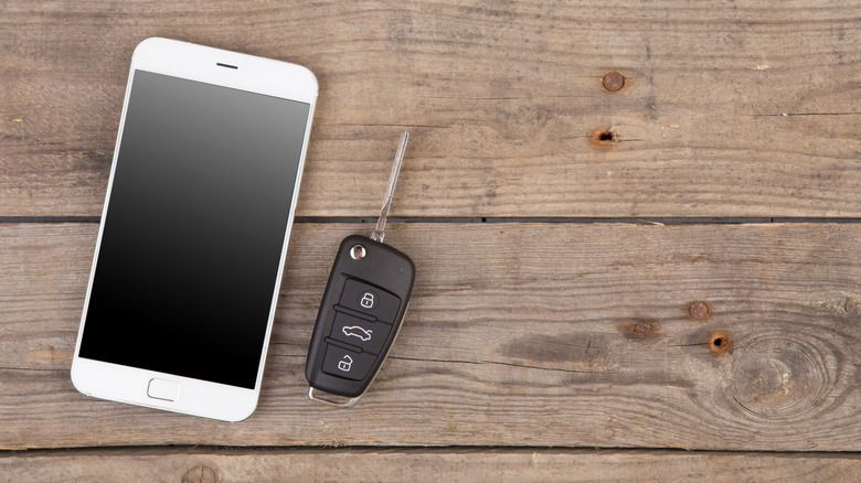 A car key next to a white phone on a wooden table
