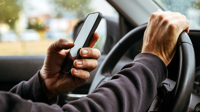 A driver holding an iPhone behind the steering wheel.