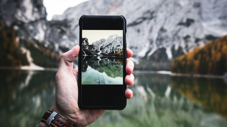 Person's hand taking photo of lake with smartphone
