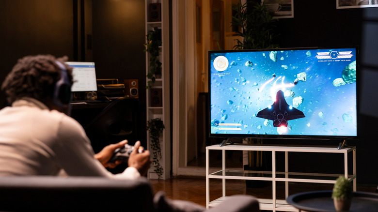 Man with a joystick in hand, playing a video game on his TV.