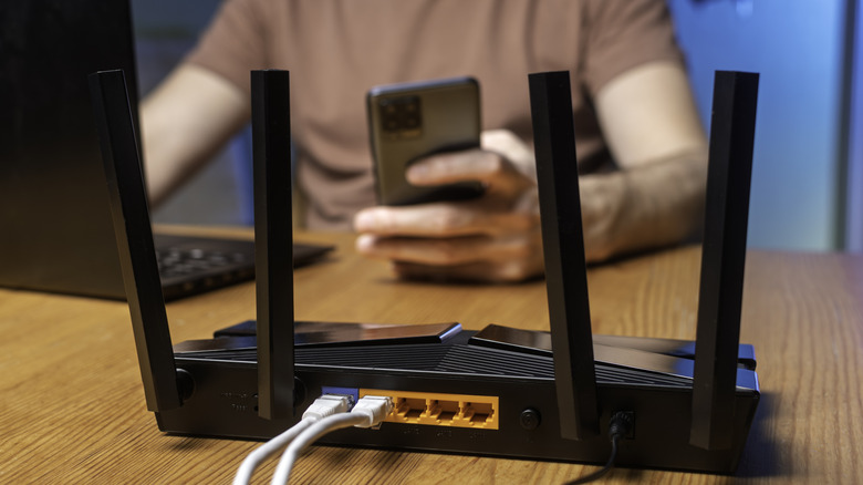 Close up of the rear of a Wi-Fi router with someone using devices in the background.