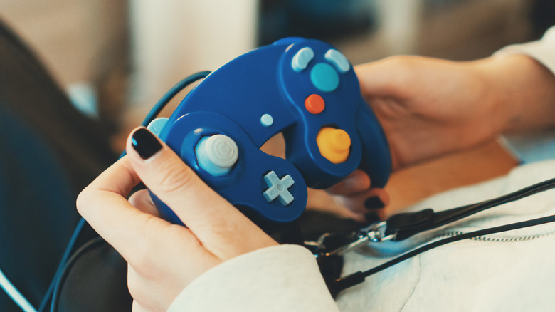 Hands holding a blue Nintendo GameCube controller with its cable resting across their lap.