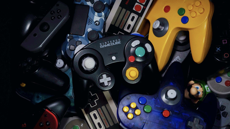 Pile of retro and modern video game controllers with a Nintendo GameCube controller in the center.
