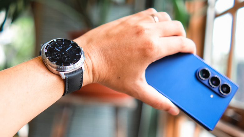 Samsung Galaxy Watch on a wrist with hand holding a phone