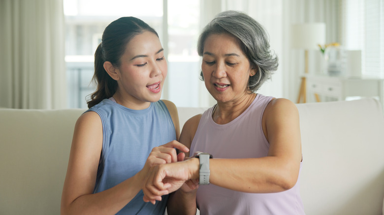 An elderly woman showing her smartwatch to a younger woman