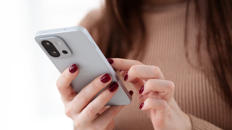 Close up of woman using a One Plus Android smartphone, the view is from the back of the device