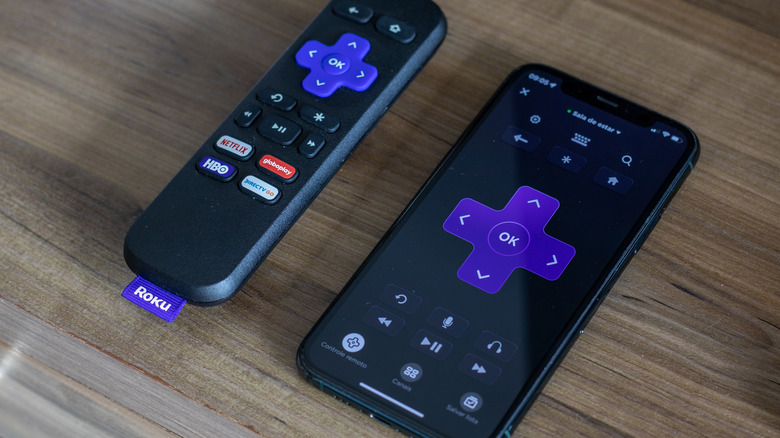 Close up of smartphone with remote app onscreen next to a Roku TV remote.