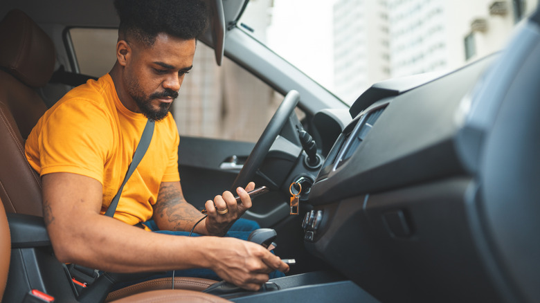 A person plugging a USB cable connected to their phone into a port in the car