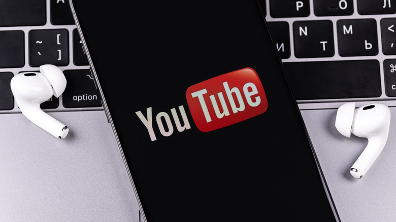 An iPhone displaying the YouTube logo as it rests a top a MacBook in between two AirPods