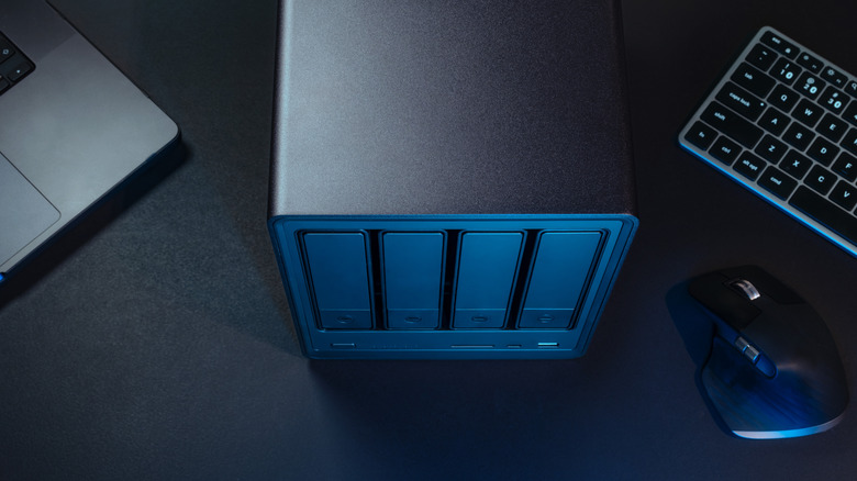 NAS server tower on an office desk with a laptop, keyboard, and mouse.