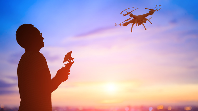 Silhouette of a man flying a drone, controller in hand at sunset.
